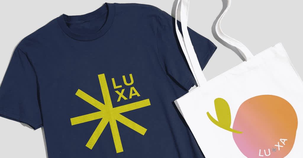 Navy T-shirt with large lime green asterisk style logo and font &ldquo;LUXA&rdquo; and a white tote bag with orange peach logo.