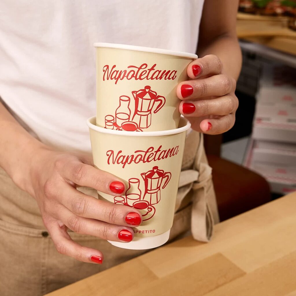 Hands holding stacked white paper cups with a red illustrated design for an Italian restaurant.