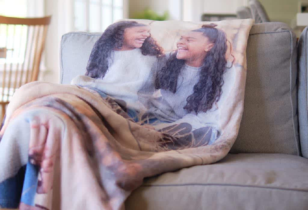 Custom photo fleece blanket draped over a couch with two sisters looking at each other and laughing.