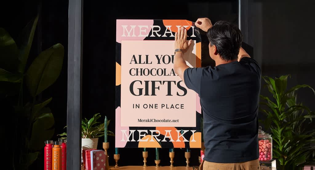 A man putting up a large poster promoting a holiday sale.