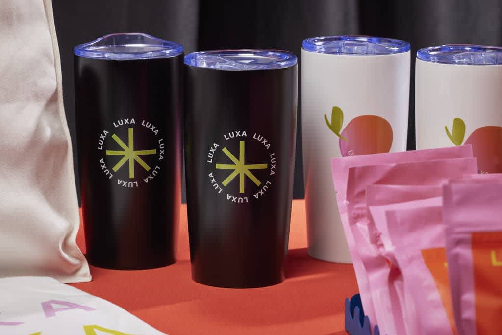 Shot of event table with selection of branded thermal tumblers  in black and white with olive and orange accents.