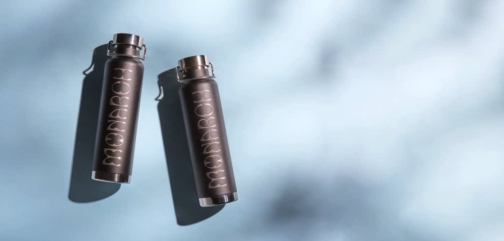 Two sleek branded water bottles with a metallic brand logo &ldquo;Monarch&rdquo; against a greying blue background.