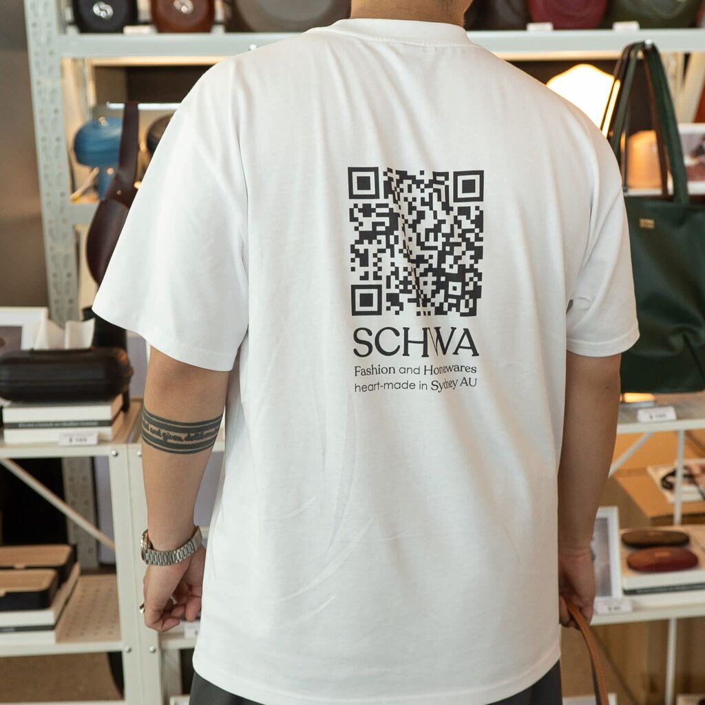 A person wearing a promotional merch T-shirt with a QR code printed on the back side.