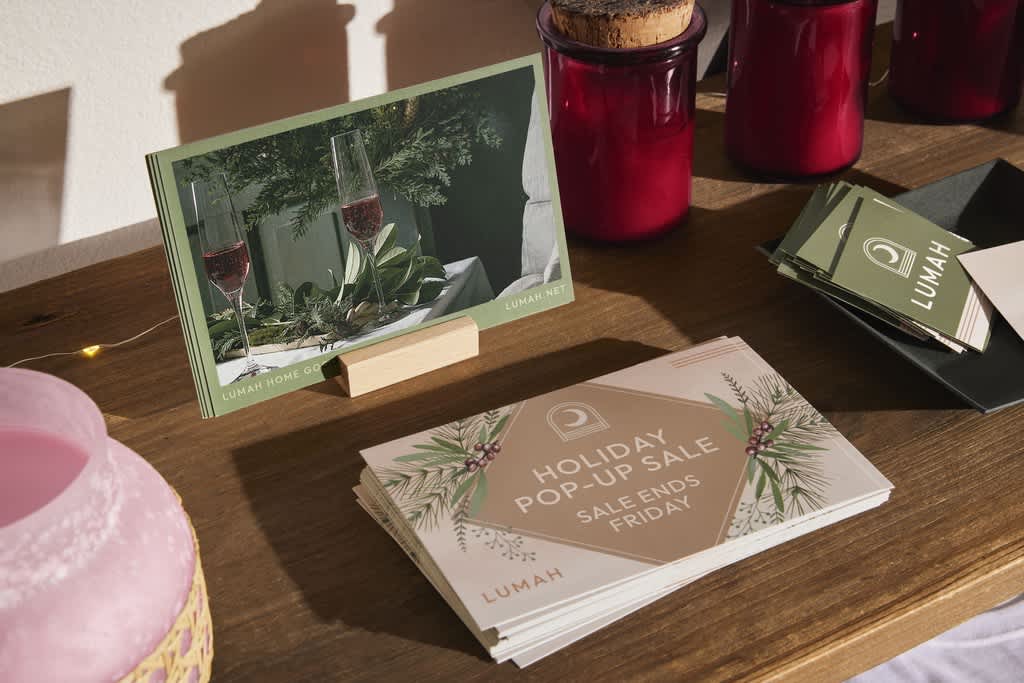 Sustainable Christmas cards promoting a holiday pop-up sale printed on recycled Christmas card paper; displayed on a wooden table with holiday décor.