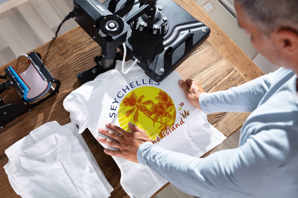 Person positioning a white T-shirt with a colorful tropical graphic underneath a heat press.