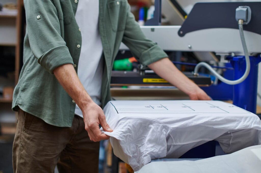 Person positioning a white garment on a printing plate in a print shop.