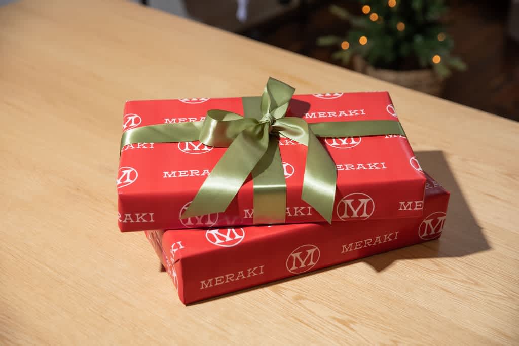 Stack of narrow boxes gift wrapped in red branded paper and green ribbon.
