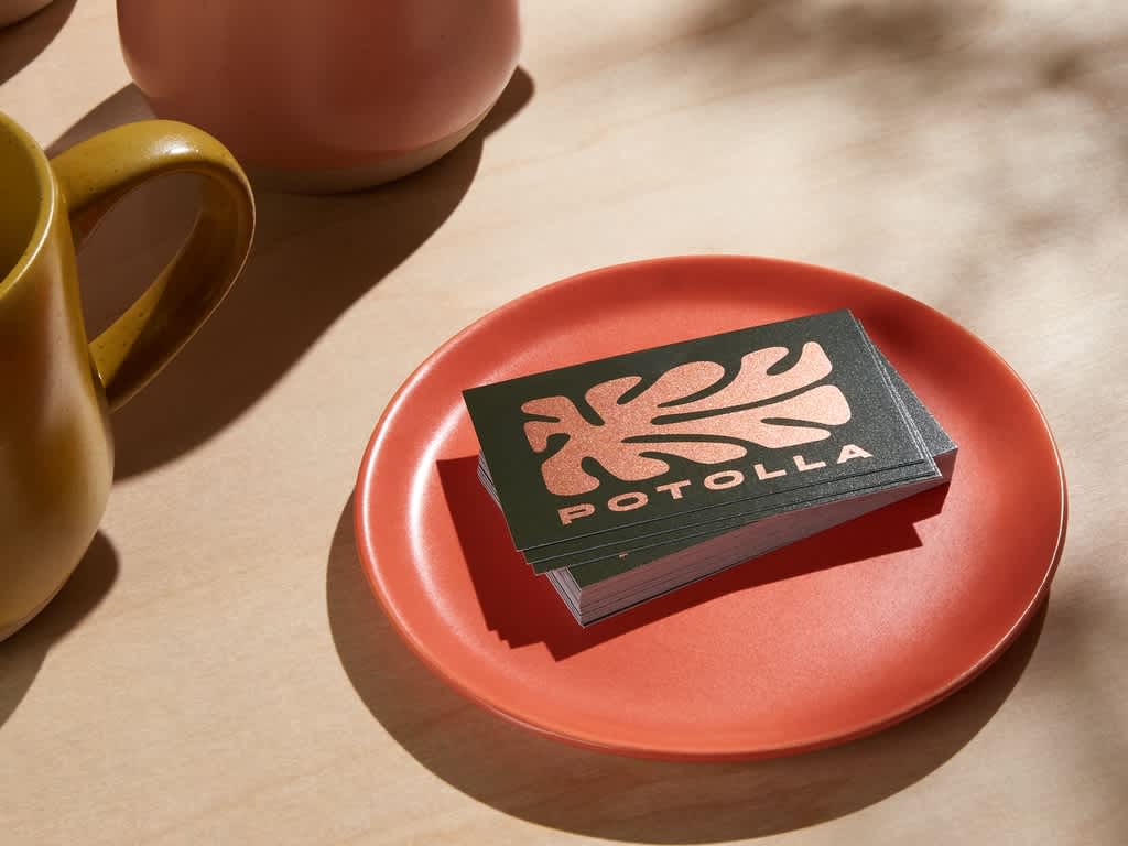 Stack of black business cards with metallic bronze organic shape logo and “Potolla” text in a red ceramic bowl.