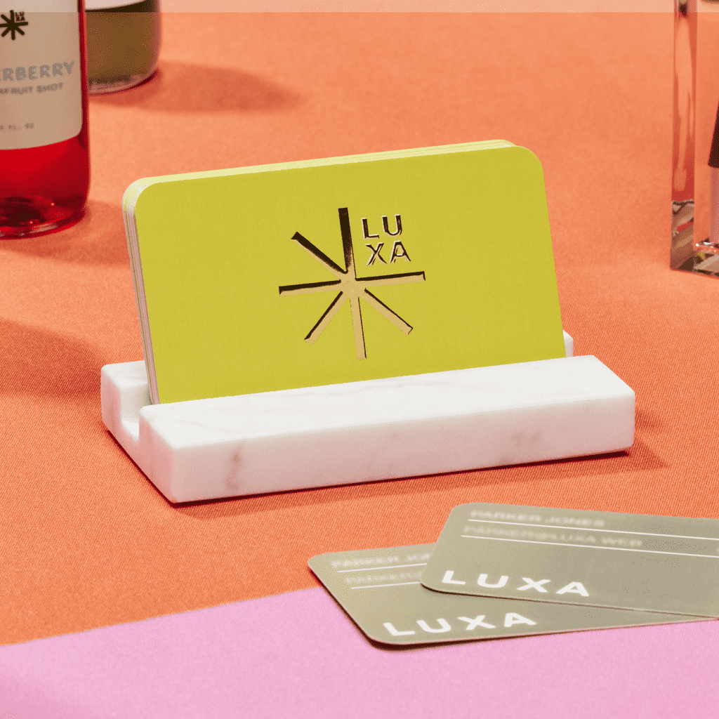 Lime green rounded edge business cards with raised gold foil star logo in a marble card holder.