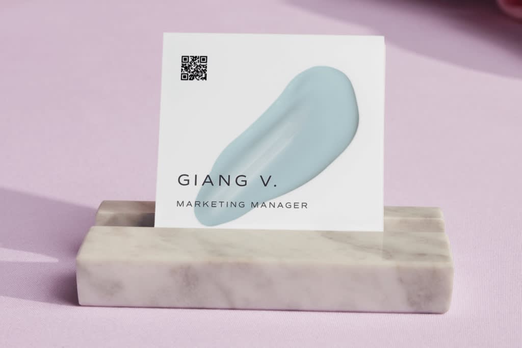 A white square business card with light blue paint smudge image, small QR code in the corner and black contact details text.