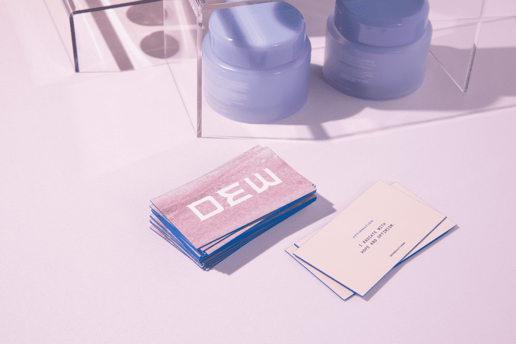 Stack of pink business cards with blue painted edges and a large white DEW logo.