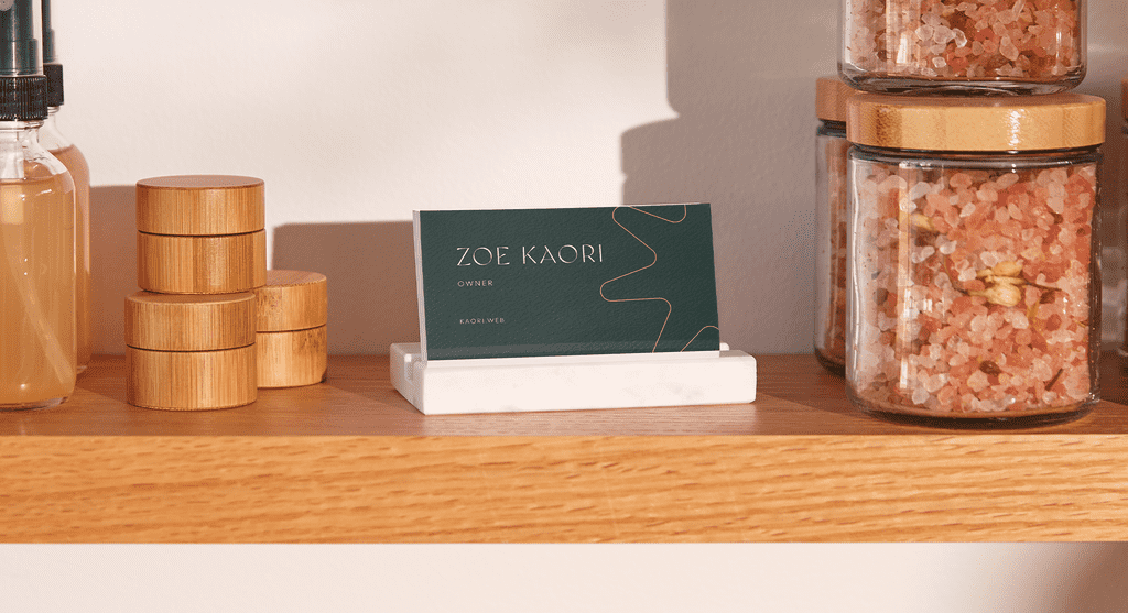 Dark green business cards with fine white contact details in a marble card holder on a wooden shelf next to products.