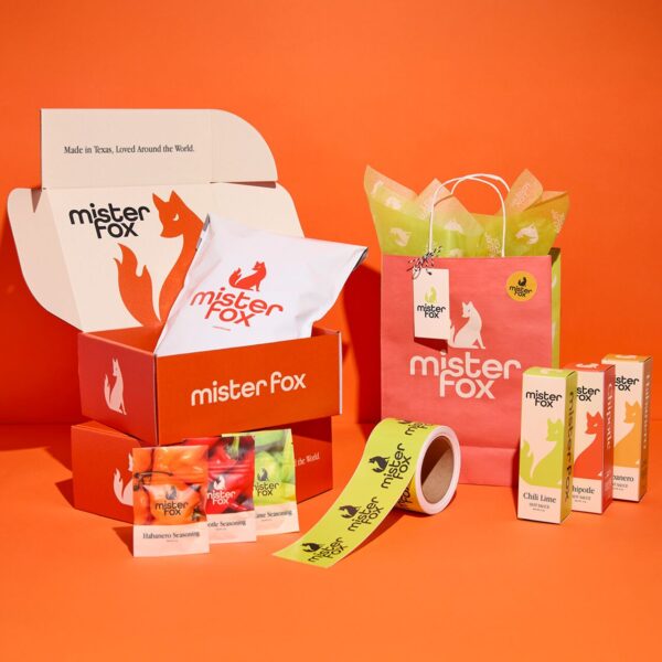Mister Fox branded packaging collection featuring an open red mailer box, custom tissue-wrapped product, paper gift bag, packaging tape and assorted seasoning products.