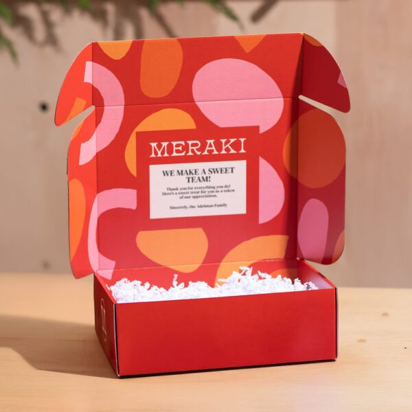 Open red and orange MERAKI custom mailer box with a printed thank-you message inside the lid and white crinkle paper filling.