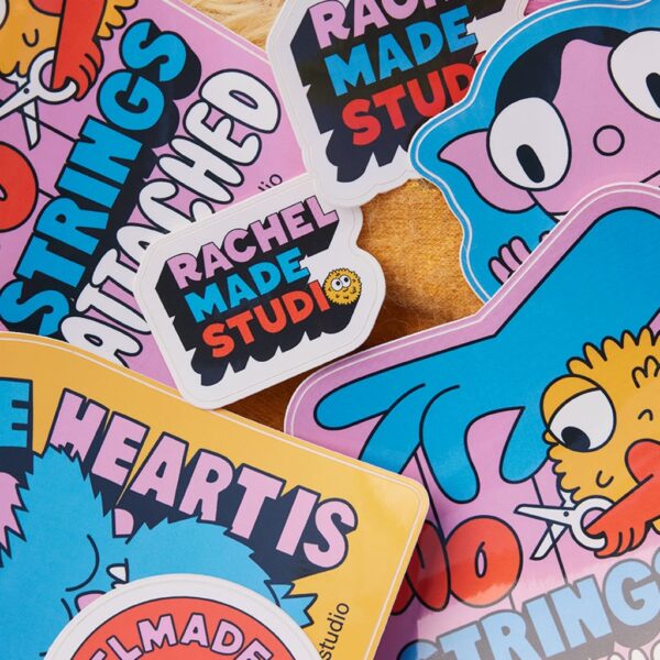 Close-up of colorful custom die-cut stickers featuring playful cartoon illustrations, bold typography and Rachel Made Studio branding.