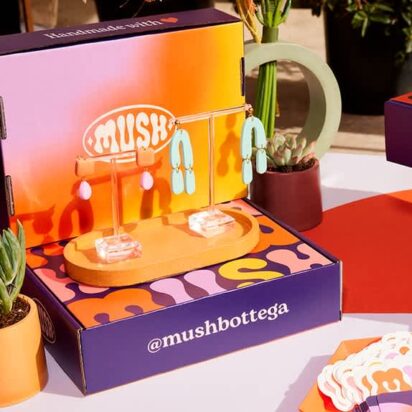 Colorful jewelry and accessories displayed on branded Mush Bottega boxes at a market stall.