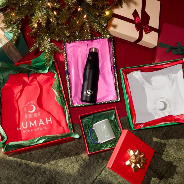Holiday gift boxes arranged beneath a Christmas tree, featuring branded apparel, a water bottle and a mug nestled in colorful tissue paper and crinkle paper filler.