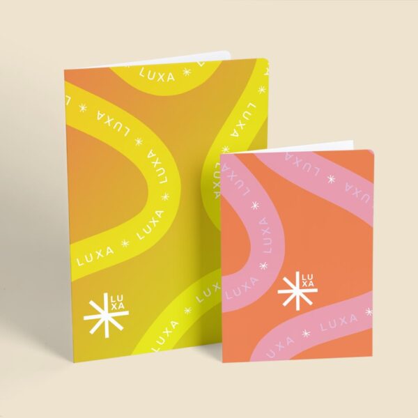 Two colorful LUXA folded cards featuring bold orange, yellow and pink patterns with repeating brand logos.
