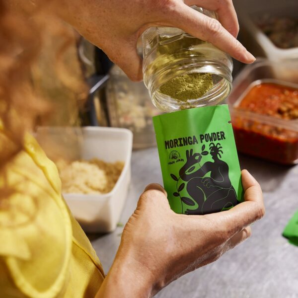 Person filling a green JAH JAH moringa powder pouch with tear notches.