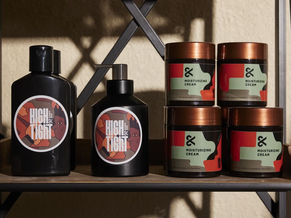 Various products on a shelf, some with large circular custom labels with graphics of people with white “High & Tight” text, the others with green and red rectangular labels with black “Moisturizing Cream” text.