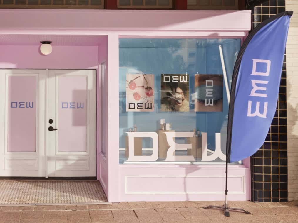 Small business storefront with feather banner in front, custom posters and products on pedestals in the window.