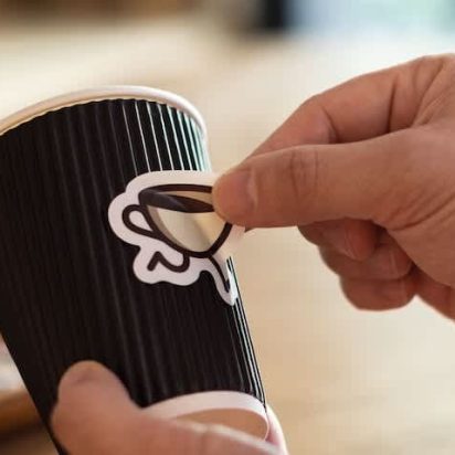A small business owner putting a die-cut custom sticker on a coffee cup