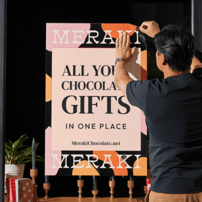 Store owner applying adhesive poster to storefront window surrounded by branded products and potted plants — signage for business in action.