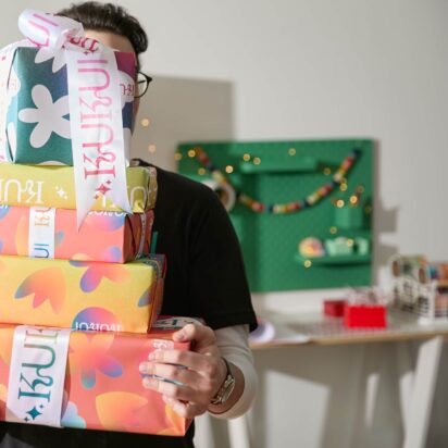 Man holding a stack of branded corporate Christmas gifts with festive lights and matching merchandise in the background