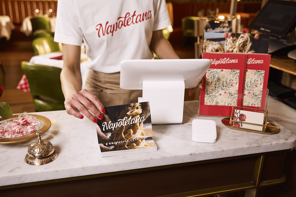 Restaurant host holding a branded postcard at a marble counter, surrounded by menus, business cards and cohesive branding design elements