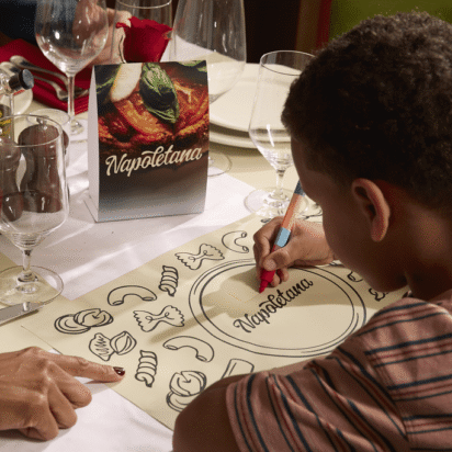 Child coloring a branded kids' placemat at a restaurant table set with Napoletana menus, table tent and printed materials