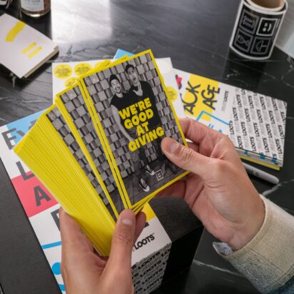 Stack of branded promotional cards with bold yellow design and marketing message held in hands over printed marketing materials