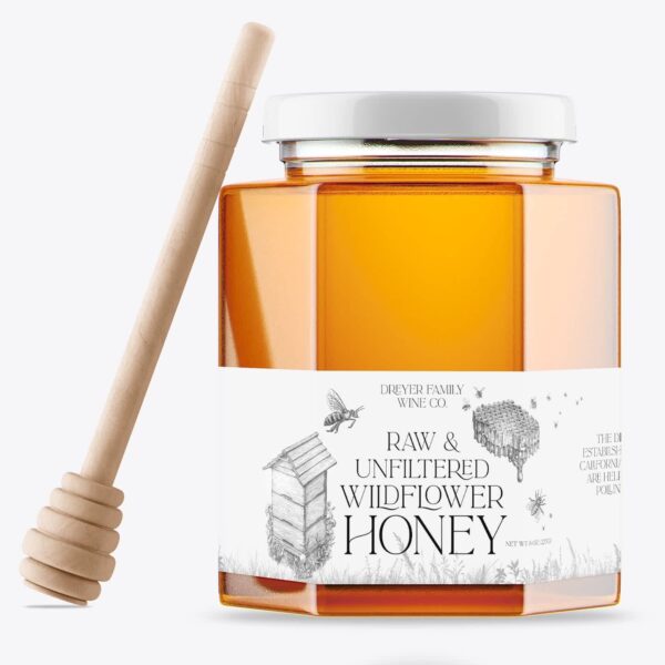 Clear glass jar of wildflower honey with white label and wooden honey dipper beside it.
