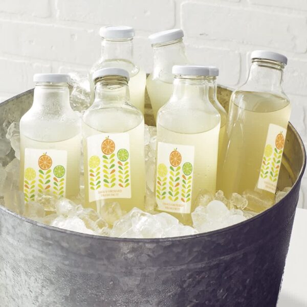 Glass bottles of fresh citrus juice with labels placed in a metal bucket filled with ice