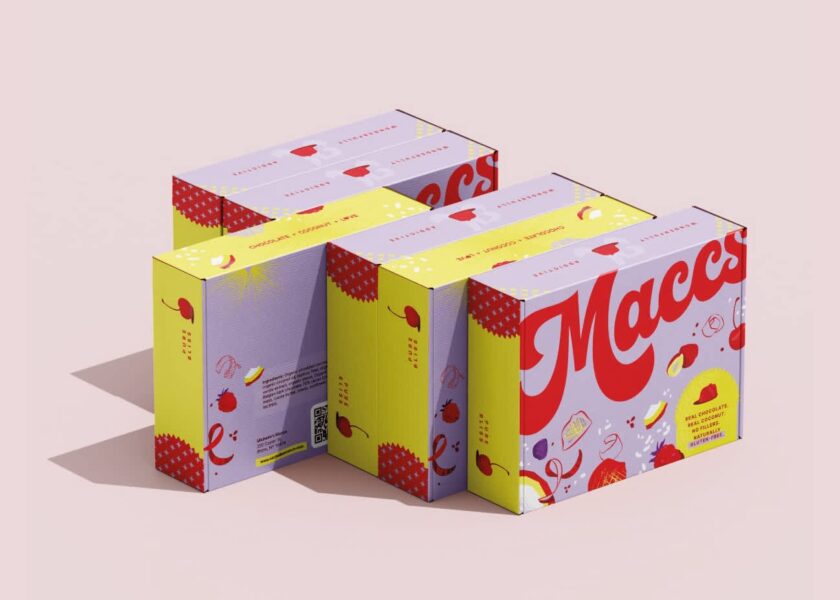 Stacked rectangular product boxes with bright yellow sides and red accents, featuring playful graphics and large &ldquo;Maccs&rdquo; logo.
