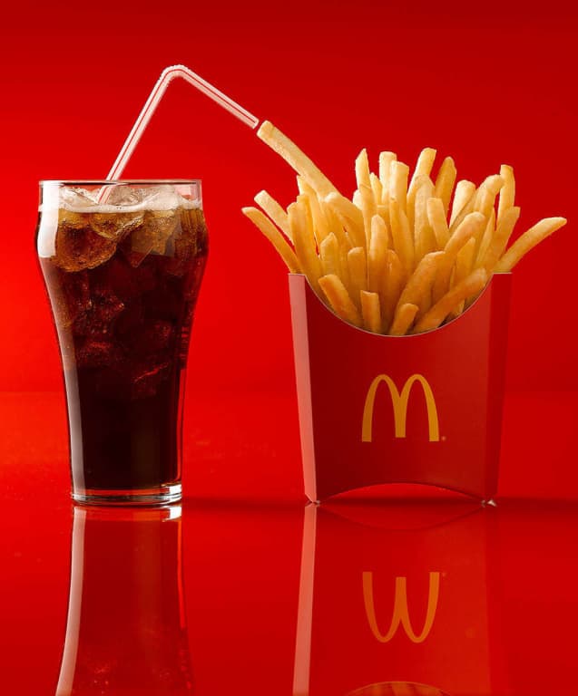 glass of coke next to a McDonald&rsquo;s french fries against a red background