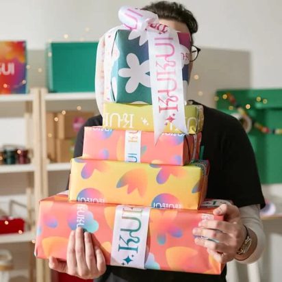 Homme portant une pile de cadeaux colorés dans ses bras, tellement nombreux qu'ils couvrent son visa