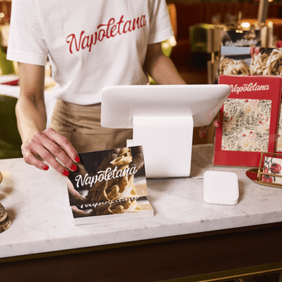 Hôte de restaurant tenant une carte postale personnalisée sur un comptoir en marbre, entouré de menus, de cartes de visite et d’éléments de design de marque cohérents.