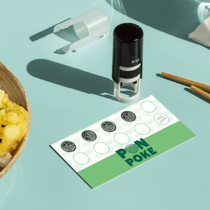 Tampon personnalisé sur une carte de fidélité à côté d’un poke bowl frais, sur un fond vert menthe.