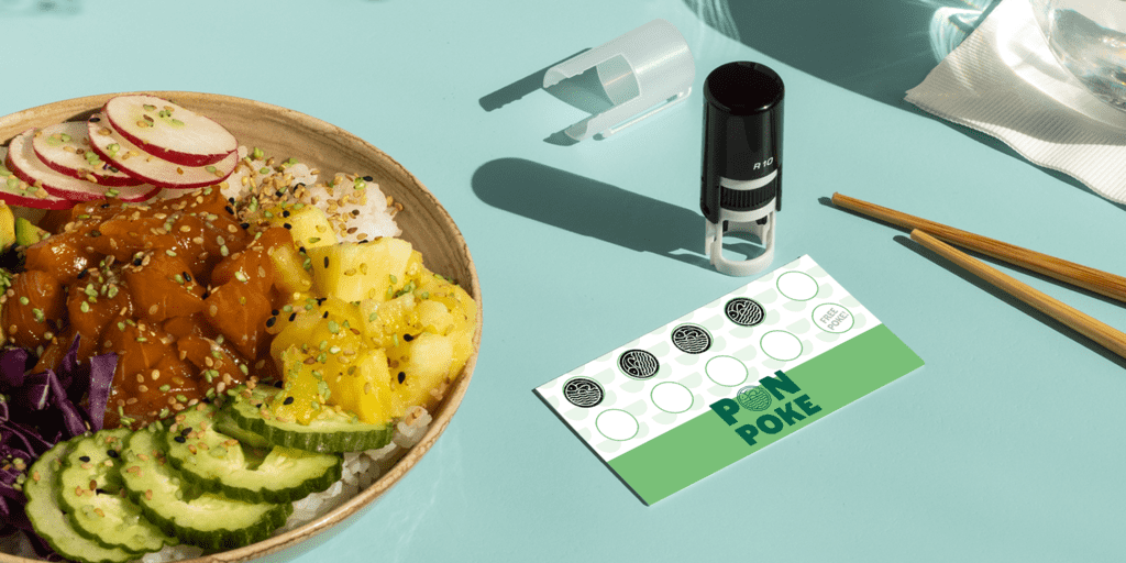 Tampon personnalisé sur une carte de fidélité à côté d’un poke bowl frais, sur un fond vert menthe.