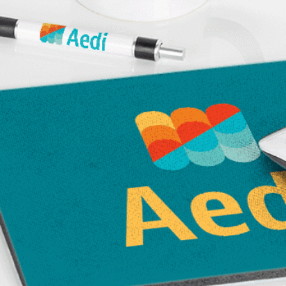 Des objets promotionnels de marque disposés sur un bureau blanc, comprenant une tasse, une clé USB, un stylo et un tapis de souris imprimés avec un logo coloré.