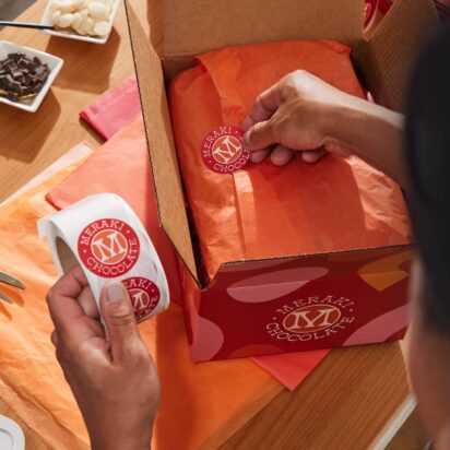 Person applying Meraki Chocolate branded stickers to holiday shipping packages.